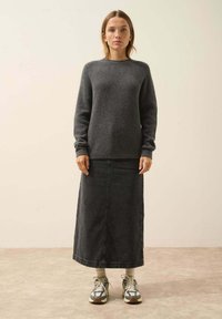 Harmaa neulepaita pitkillä hihoilla, yhdistettynä pitkä tummansinisellä farkkuhameella. Mallilla on harmaat sukat ja moniväriset lenkkitossut. Neutraali tausta.