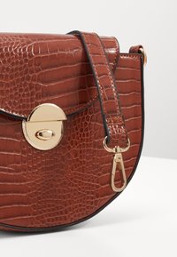 Borsa a mezzaluna in pelle marrone con motivo coccodrillo, chiusura a girello in metallo dorato e tracolla removibile con clip dorata.