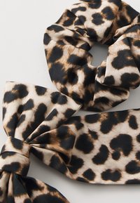 Scrunchie i mašna sa printom leoparda izrađeni od mekane tkanine, s kombinacijom bež, smeđe i crne boje u teksturiranom uzorku.