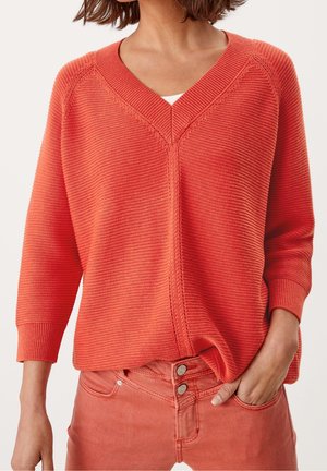 Leichter, lebhaft orangefarbener Pullover mit V-Ausschnitt und geripptem Muster. Hat Dreiviertelärmel und einen lockeren Schnitt, kombiniert mit rosa Jeans.