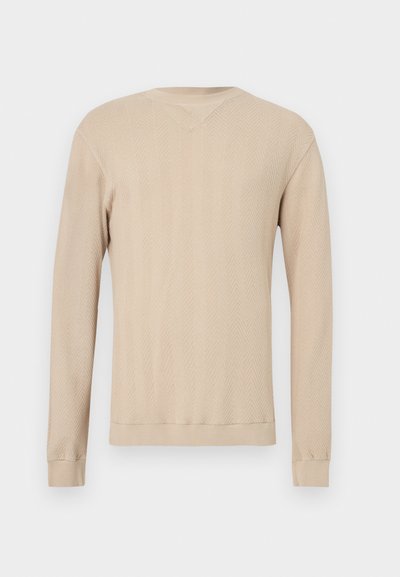 Pull beige à manches longues avec un motif en chevrons, doté d'un col en V, de poignets côtelés et d'un design en tricot texturé. Tissu doux.