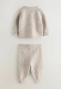 Conjunto de dos piezas que incluye un suéter de punto beige de mangas largas y un par de pantalones ajustados a juego, ambos con puños acanalados.