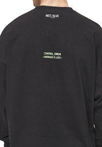 Sudadera negra con cuello redondo y corte relajado. En la parte posterior se muestra un texto verde: "CONTROL_ERROR <AVERAGE IS LOST>" con un logo encima.