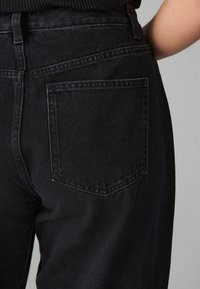 Črne denim hlače z zadnjim žepom z nežnim šivom, gladko teksturo in visokim pasom.