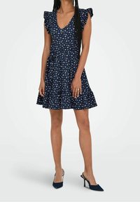 Navy blumenkleid mit V-Ausschnitt, Rüscheärmeln, taillierter Taille und gestuftem Rock. Kombiniert mit schwarzen, hohen Mules. Baumwollstoff, leichtes Material.