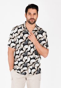 Camisa de botones de manga corta con un patrón geométrico en negro, blanco y beige, con formas contrastantes y una textura de tela suave.