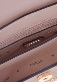 Interno della borsa colore rosa chiaro con una tasca con cerniera, rivestimento morbido e il marchio "GUESS" visibile. Presenta cuciture pulite e accenti sottili.