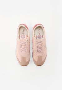 Jasnoróżowe zamszowe trampki z postrzępionymi akcentami, teksturowanymi panelami, okrągłymi sznurowadłami i gumową podeszwą. Na języku znajduje się logo.