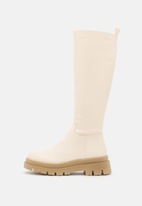 Botas de creme até ao joelho, feitas de material suave, com uma sola robusta em bege, com sulcos profundos e uma pequena pega na parte superior.