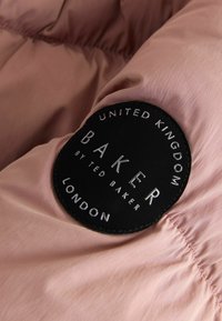 Patch circolare nero del marchio Baker London cucito su un tessuto trapuntato rosa, che mostra il nome del marchio e il testo di origine.