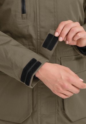 Chaqueta de color verde oliva con cierres de velcro en los puños, con costuras visibles y dos bolsillos frontales. Textura de tela suave y duradera.