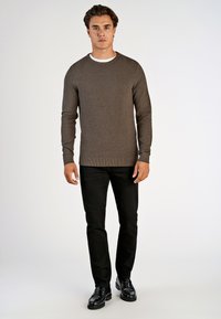 Ruskea neulepaita, jossa on pyöreä kaulus, ribbireunukset ja tekstuuripinta, yhdistetty mustiin slim fit -housuihin ja kiiltäviin mustiin kenkiin.