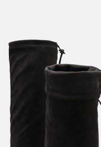 Botas de ante negro con una textura suave, que presentan un cierre de cordón en la parte superior y un diseño simple y sin adornos.