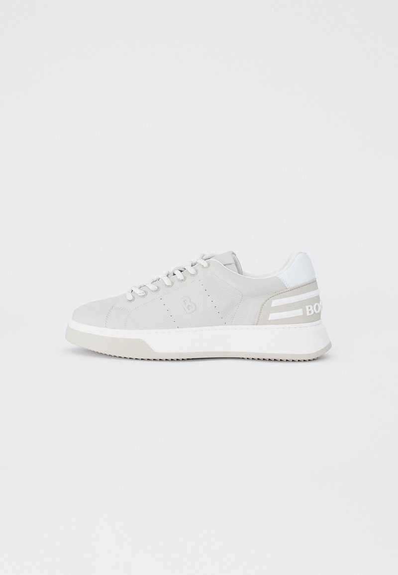 Baskets basses gris clair avec semelle blanche, lacets et patch au talon, avec un logo discrètement embossé sur le côté et des détails rayés au talon.