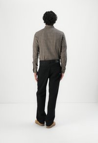 Camisa a cuadros marrón y beige, de mangas largas, pantalones de mezclilla negros, ajuste recto, combinada con zapatos marrones claro, vista desde la parte trasera.