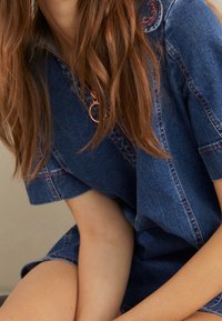 Denimöveralls med korta ärmar, med dragkedjesslutning och kontrasterande sömmar. Mjuk textur i en klassisk blå färg.