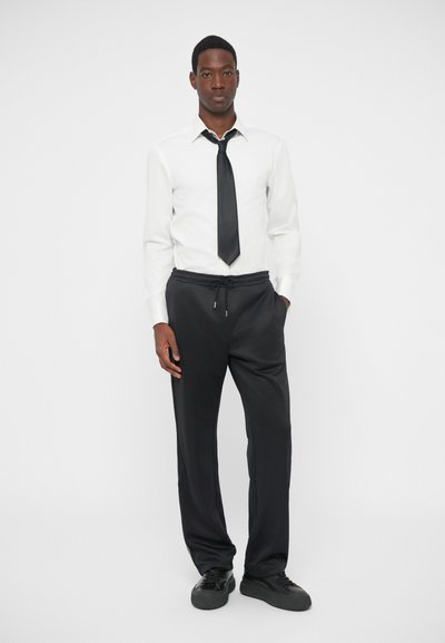 White long-sleeve shirt with a black tie, paired with black drawstring pants and black sneakers. Simple, tailored design with a relaxed fit.