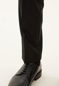 Pantaloni neri con taglio aderente, abbinati a scarpe di pelle nera con texture, dotate di lacci e tacco rialzato. Tessuto liscio con dettagli minimi.