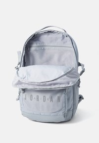 Light gray backpack with a mesh front pocket, zippered compartments, and adjustable straps. Features "JORDAN" in block letters.
