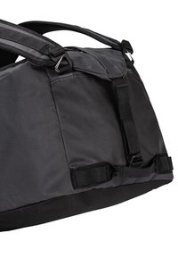Zwarte nylon sporttas met een getextureerde oppervlakte, verstelbare banden, zijgespen en een stevige basis met een versterkte bodem.