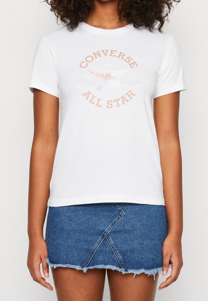 T-shirt en coton blanc avec un motif central multicolore d'une étoile accompagné du texte "Converse All Star". Associé à une jupe en jean.