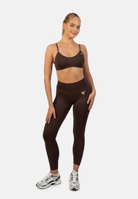 Ruskea urheil bra ja siihen sopivat korkeavyötäröiset leggingsit joustavaa materiaalia. Varustettu logodetaililla vasemmalla puolella ja mukautetulla designilla mukavuutta varten.