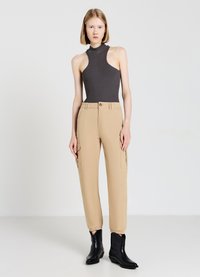 Grauer ärmelloser Bodysuit kombiniert mit hellbeigen Cargo-Hosen, die Seitentaschen, elastische Bündchen und schwarze Knöchelboots haben.