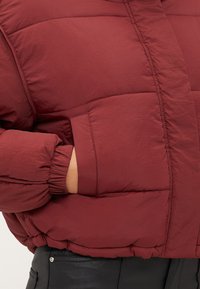 Bordowa kurtka puchowa z pikowanym wzorem, ściągaczami na rękawach i bocznymi kieszeniami, wykonana z miękkiego, strukturalnego materiału i o dopasowanym kroju.