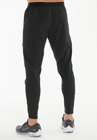 Schwarze Sporthosen mit einer schmalen Passform, elastischem Bund und kontrastierenden schwarzen Unterschenkeln. Kombiniert mit grauen Laufschuhen.