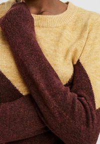 Maglione lavorato a maglia con un corpo giallo e maniche diagonali color maroon, e collo a coste. Texture morbida con colori sfumati e vestibilità comoda.
