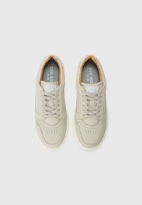 Zapatillas beige con parte superior de cuero suave, punta redonda, detalles perforados y cuello acolchado; cordones redondos y suela de goma blanca.