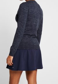Navy textured knit sweater with long sleeves and a fitted waist, paired with a dark blue, flared athletic skirt featuring a logo detail.