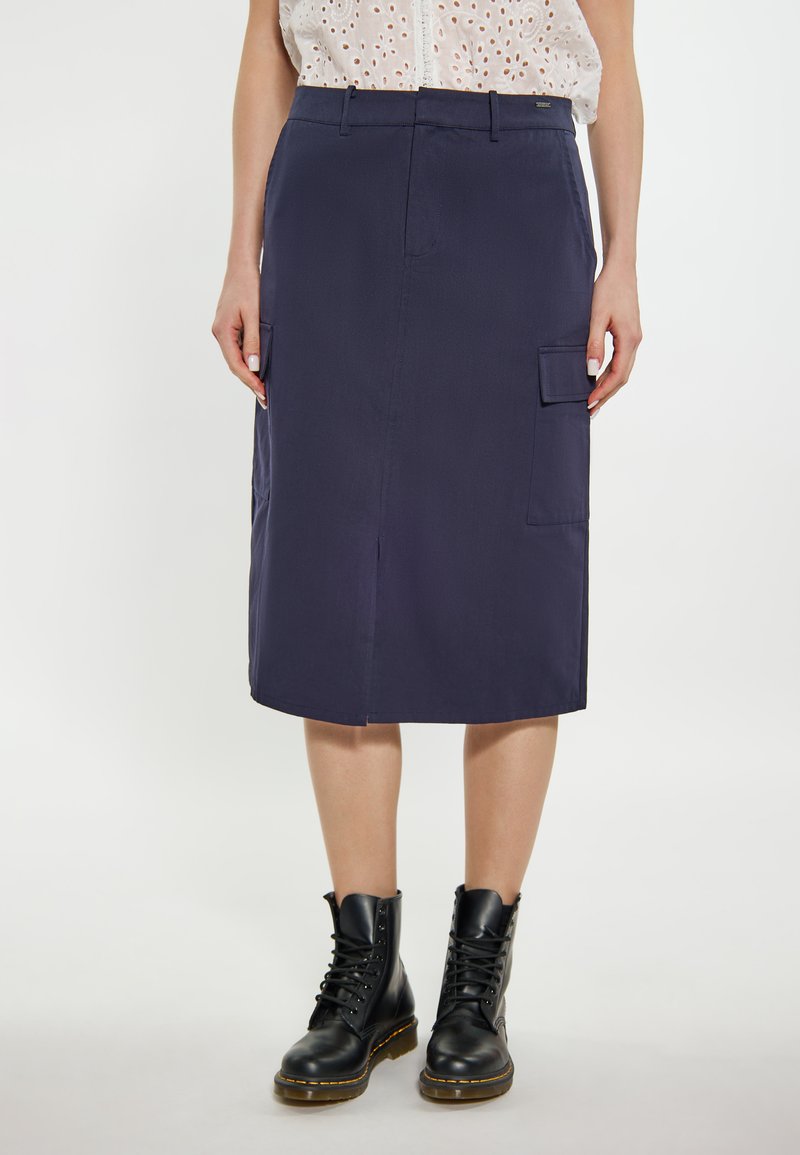 Robe midi bleu marine en tissu léger, avec une coupe droite, des poches inclinées et une fente avant. Associée à des bottes à lacets noires.