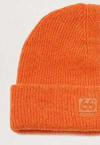 Oranssi neulospipo, jossa on uritettu pinta ja taitettu reuna. Edessä on pieni brodeerattu logotagi, jossa lukee "66° N".
