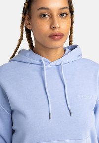 Hoodie azzurro chiaro con tasca frontale, cappuccio con cordini e logo ricamato. Tessuto liscio con vestibilità comoda e polsini a coste.