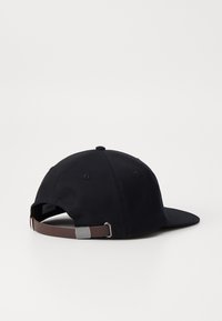 Black cotton cap featuring a curved brim, adjustable brown strap with metal hardware at the back, and embroidered ventilation eyelets.