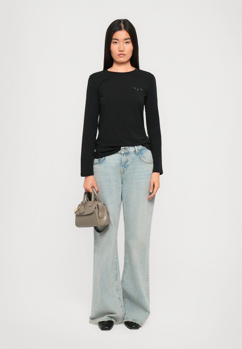 T-shirt nera a maniche lunghe con design minimalista, jeans baggy azzurri e una piccola borsa grigia. L'outfit presenta uno stile casual.