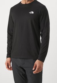 Schwarzes Langarm-T-Shirt aus Baumwolle mit Rundhalsausschnitt. Verfügt über ein weißes Logo auf der linken Brustseite und eine glatte, weiche Textur.