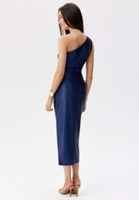 Jednobodový námořnický saténový šaty s přiléhavým živůtkem, do délky po lýtka a hladkým povrchem. Má zřasené detaily na zadní straně.