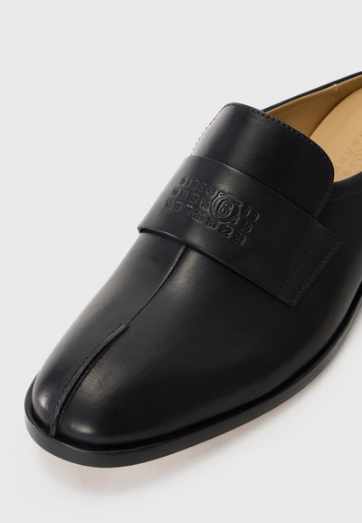 Svart läderloafers med sydd delad tå och präglade siffror på den breda remmen över den övre framdelen.