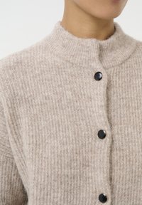 Beige gebreide cardigan met een hoge kraag, voorzien van een geribbeld patroon en zwarte ronde knopen als sluiting. Close-up afbeelding van de stof.