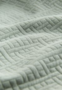 Tissu gris clair doux avec un motif géométrique en relief composé de formes rectangulaires entrelacées et de lignes.