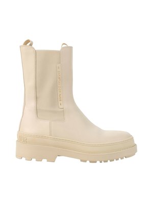 Bottine beige en cuir avec semelle épaisse, panneau latéral élastique, languettes de tirage et marquage embossé "Christian Dior Paris" sur le côté.