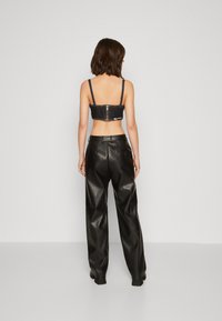 Top corto in denim nero con spalline regolabili e una zip metallica sul retro, abbinato a pantaloni larghi in ecopelle nera.