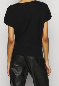 Schwarzes Strickoberteil mit kurzen Ärmeln und gerippter Textur, ausgestattet mit einem weiten Ausschnitt und einem enganliegenden Saumband. Kombiniert mit schwarzen, lederähnlichen Hosen.