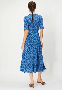 Sininen kukallinen midi-mekko, jossa on lyhyet hihat, vyötäröltä kiristetty malli ja levenevä helma. Mekossa on kirkas sininen väri ja sileä kangas.