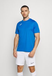 Modré sportovní tričko s krátkým rukávem a kulatým výstřihem, s bílým logem. V kombinaci s bílými šortkami a ponožkami. Hladká textilie.