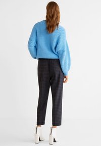 Jasnoniebieski sweter z grubym splotem i opadającymi ramionami, w połączeniu z ciemnymi spodniami w kratę o zwężanych nogawkach oraz białymi botkami za kostkę na zamek.