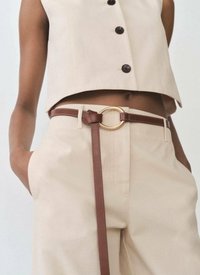 Beige kort topp med svarta knappar, ihop med beiga byxor. Brunt läderbälte med ett cirkulärt guldspänne och en hängande rem.