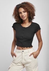 T-shirt noir à côtes, court, avec un col rond et des manches courtes à volants, présentant une rangée de boutons noirs sur le devant.